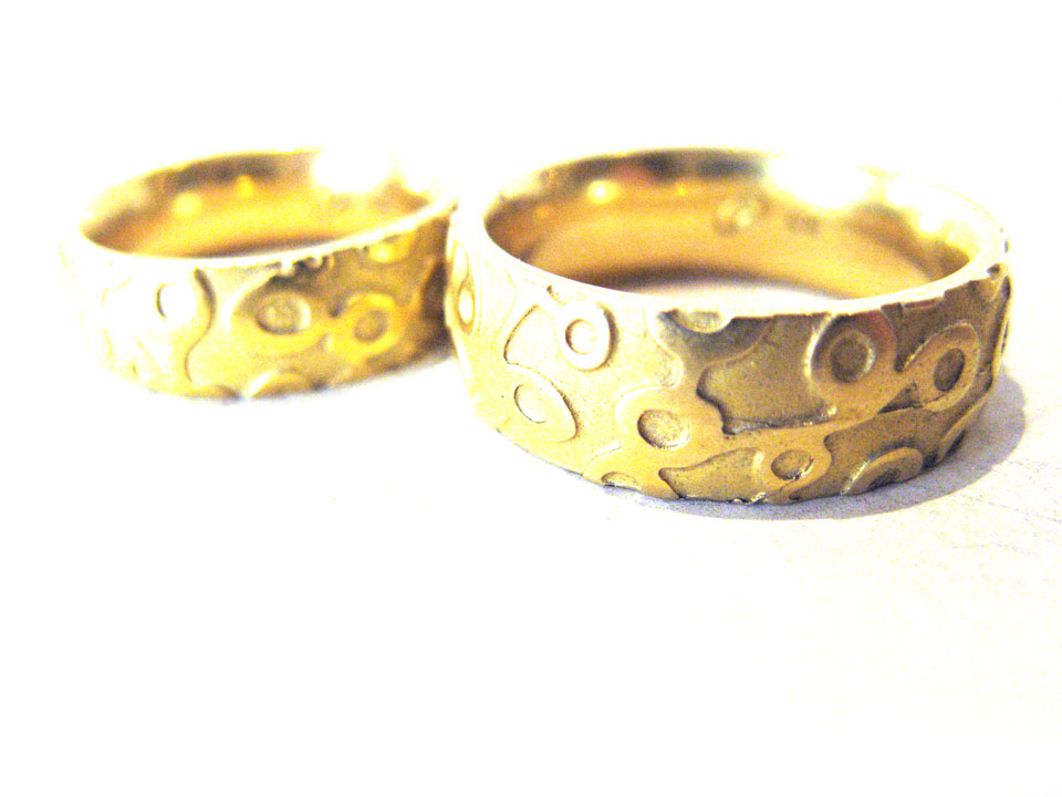 Trauringe anders in Gelbgold: Aus der Außenfläche dieser Ringe hebt sich ein grafisches Muster, eine Art "Kringel-Struktur".